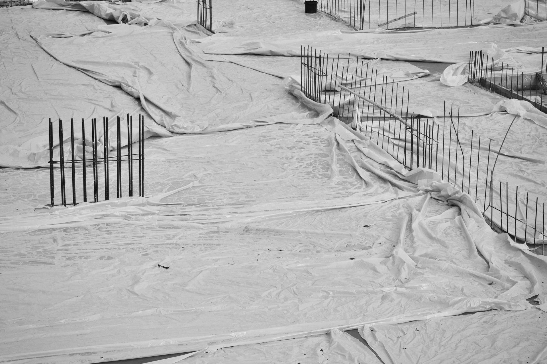 Monochrome image of a construction site with foundations covered by sheets and exposed rebar.